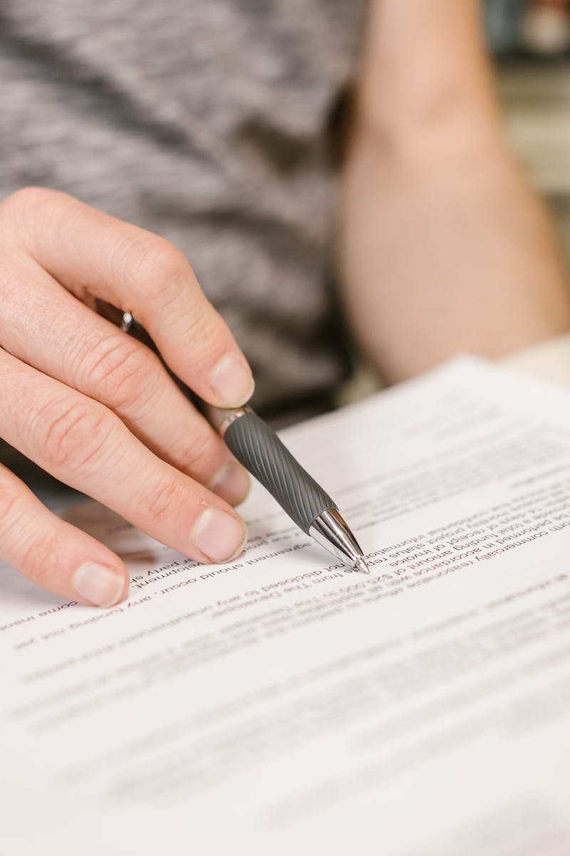 Close-up of a person's hand signing an important legal document with a pen indoors.